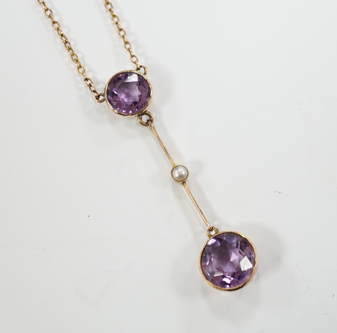 An Edwardian 9ct, two stone amethyst and single stone seed pearl set drop pendant necklace, gross weight 3.8 grams.